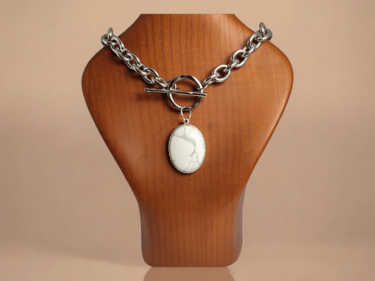 A white Howlite pendant on a chunky chain on a wooden bust Main image
