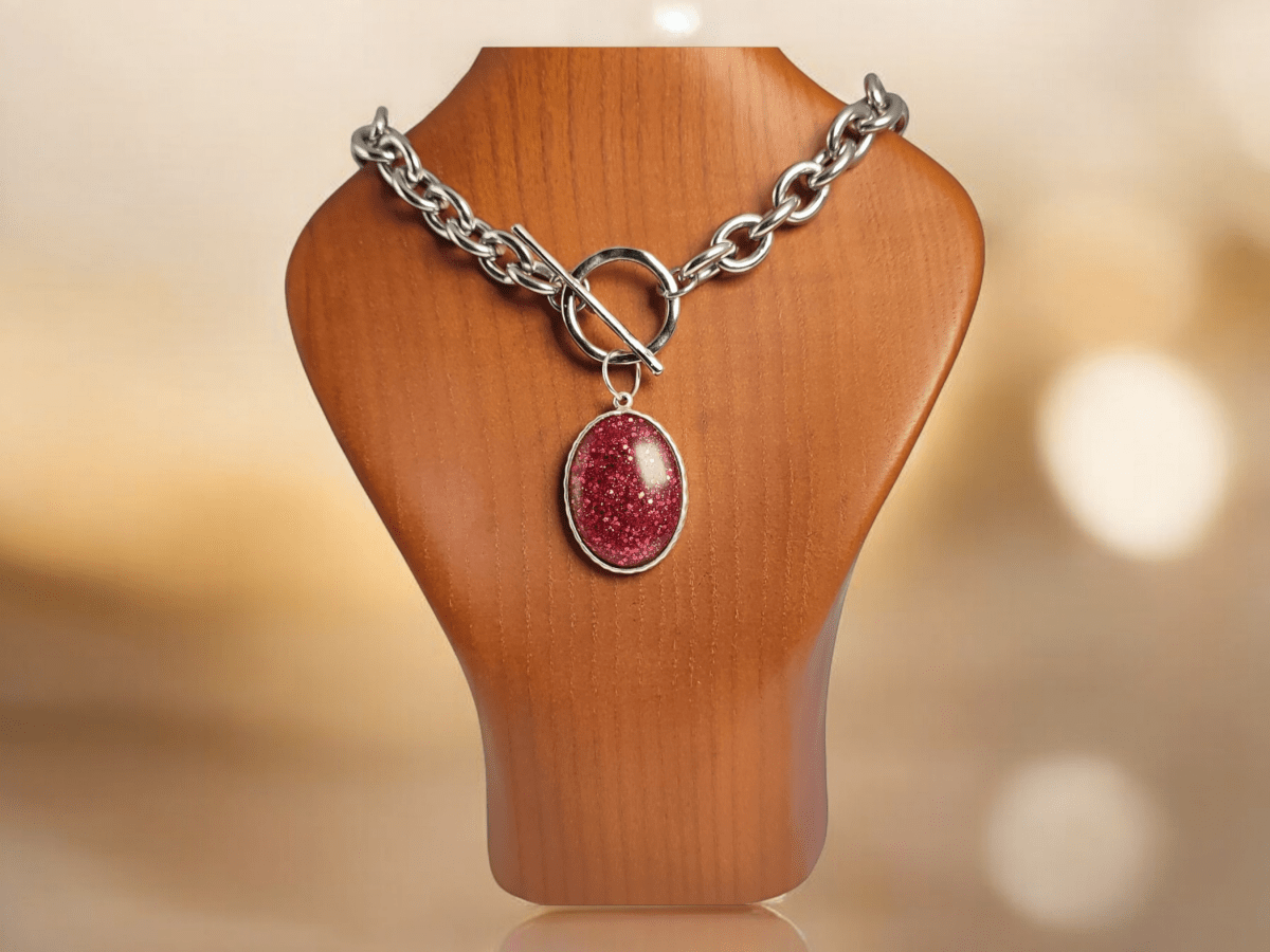 A red glitter pendant on a chunky chain on a wooden bust Main image