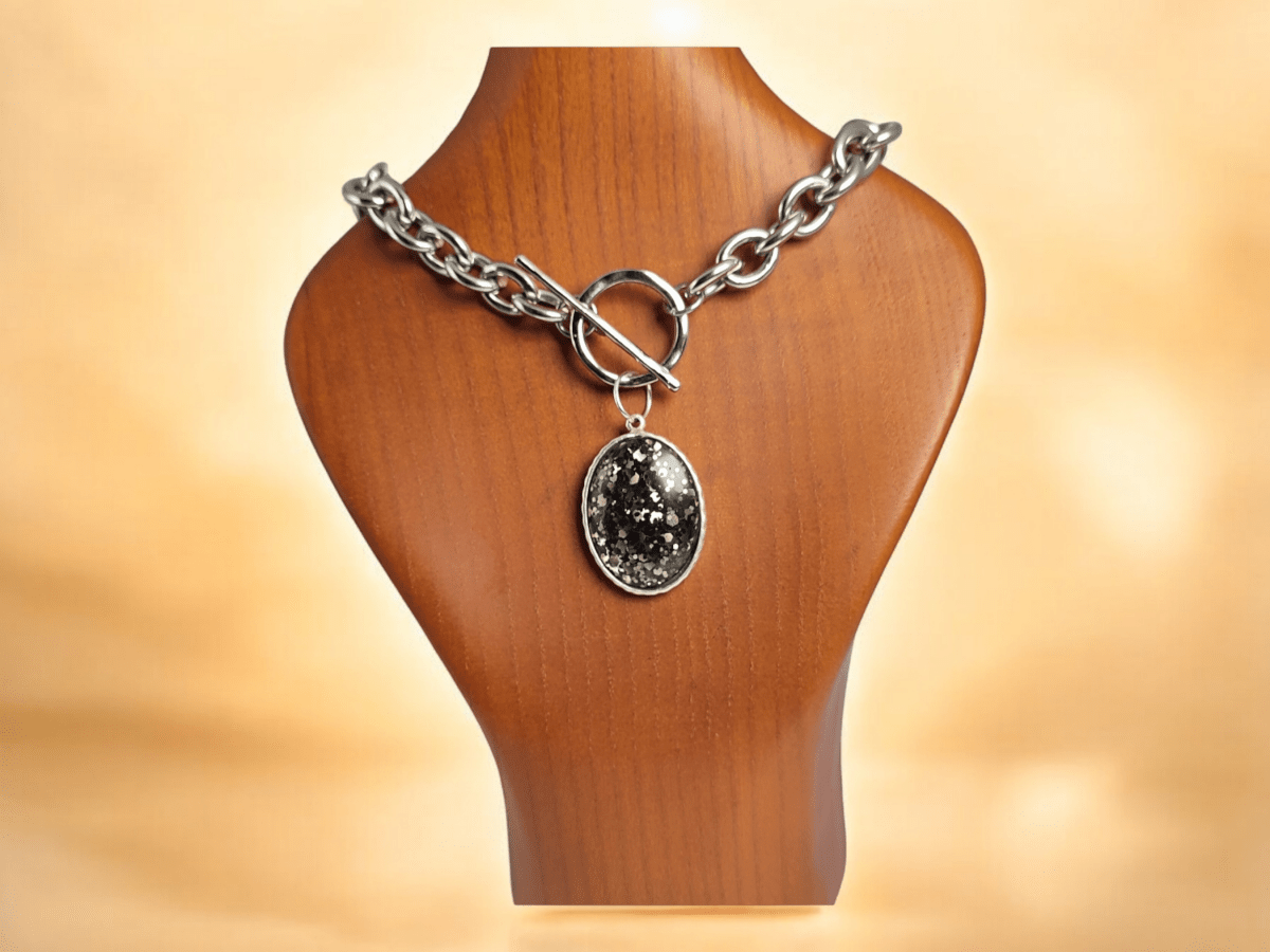 A black sparkly pendant on a chunky silver chain on a wooden bust