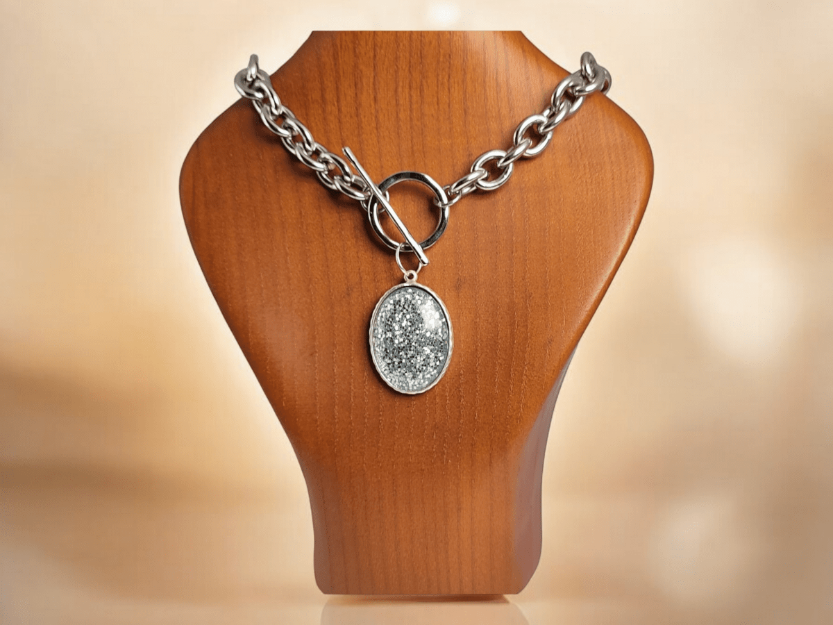 A large silver glitter pendant suspended from a chunky chain on a wooden bust