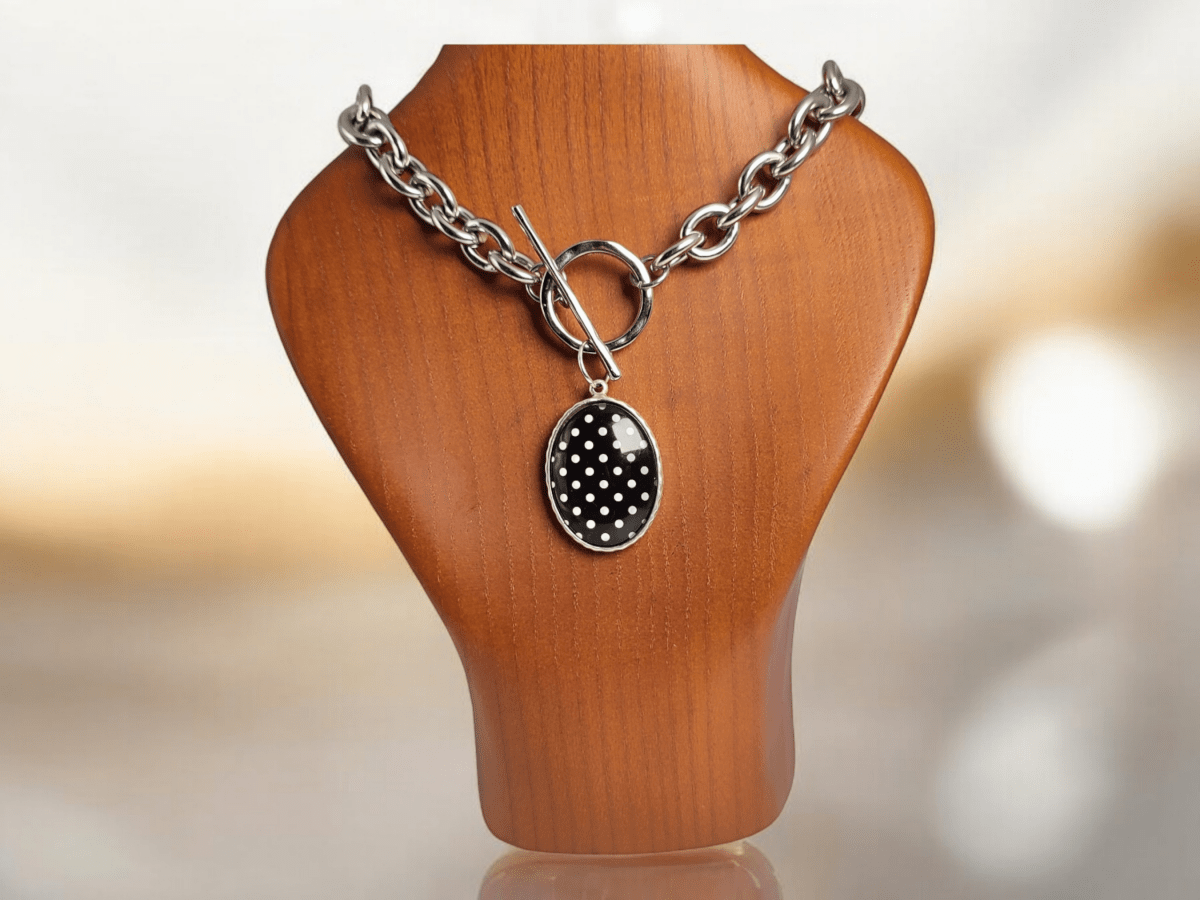 A black and white polka dot pendant on a chunky chain on a wooden bust Main image