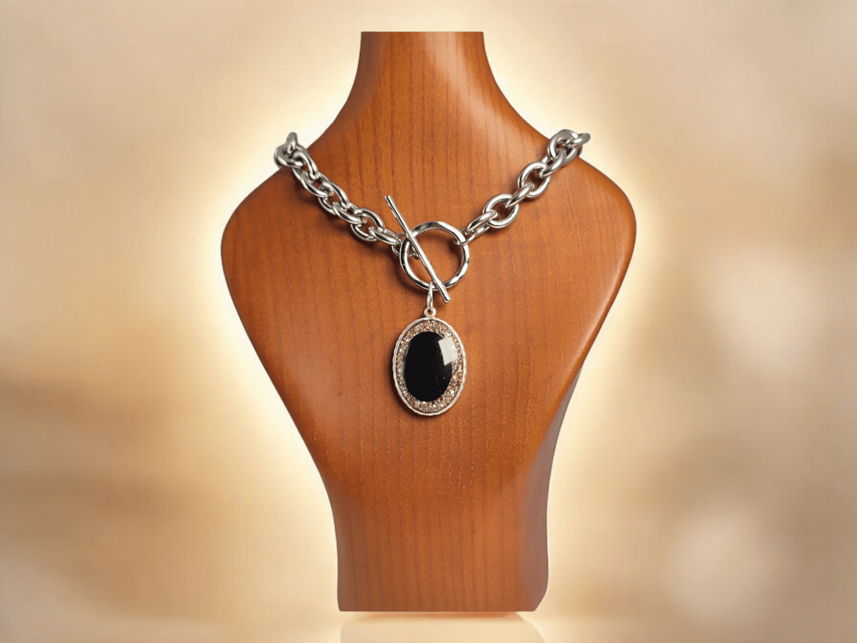 A black gold and silver glitter pendant o a chunky chain on a wooden bust