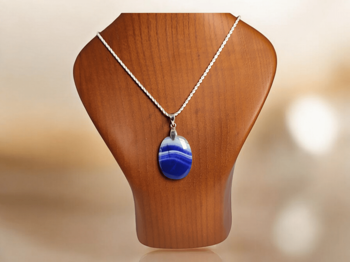 A blue Agate pendant suspended from a silver chain on a wooden bust