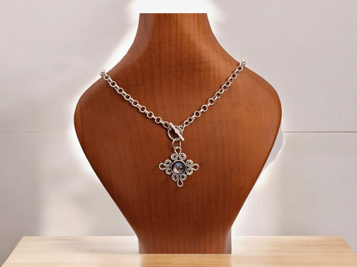 A vintage style pendant on a chain on a wooden bust