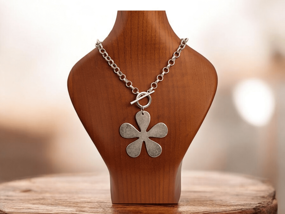 A large silver flower pendant on a wooden bust