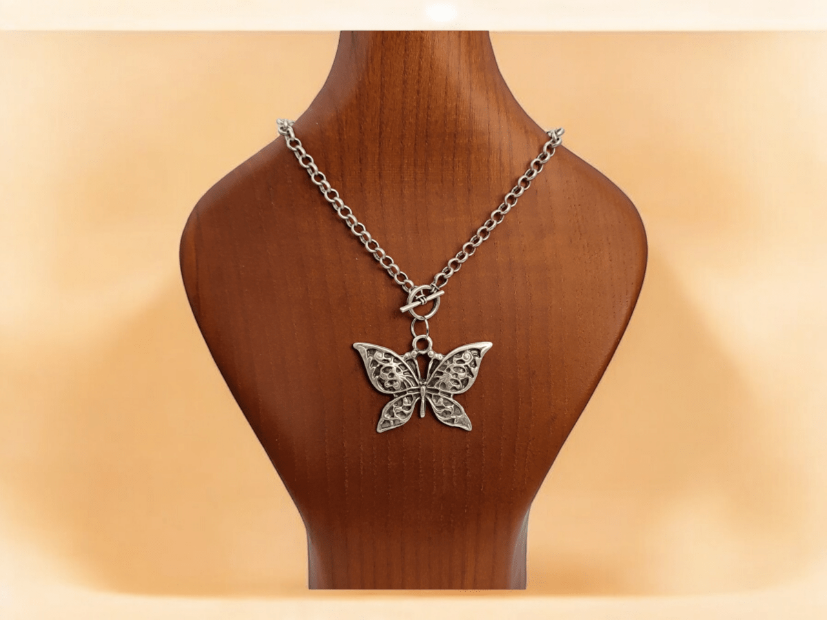 A silver butterfly pendant suspended from a silver chain on a wooden bust Main image