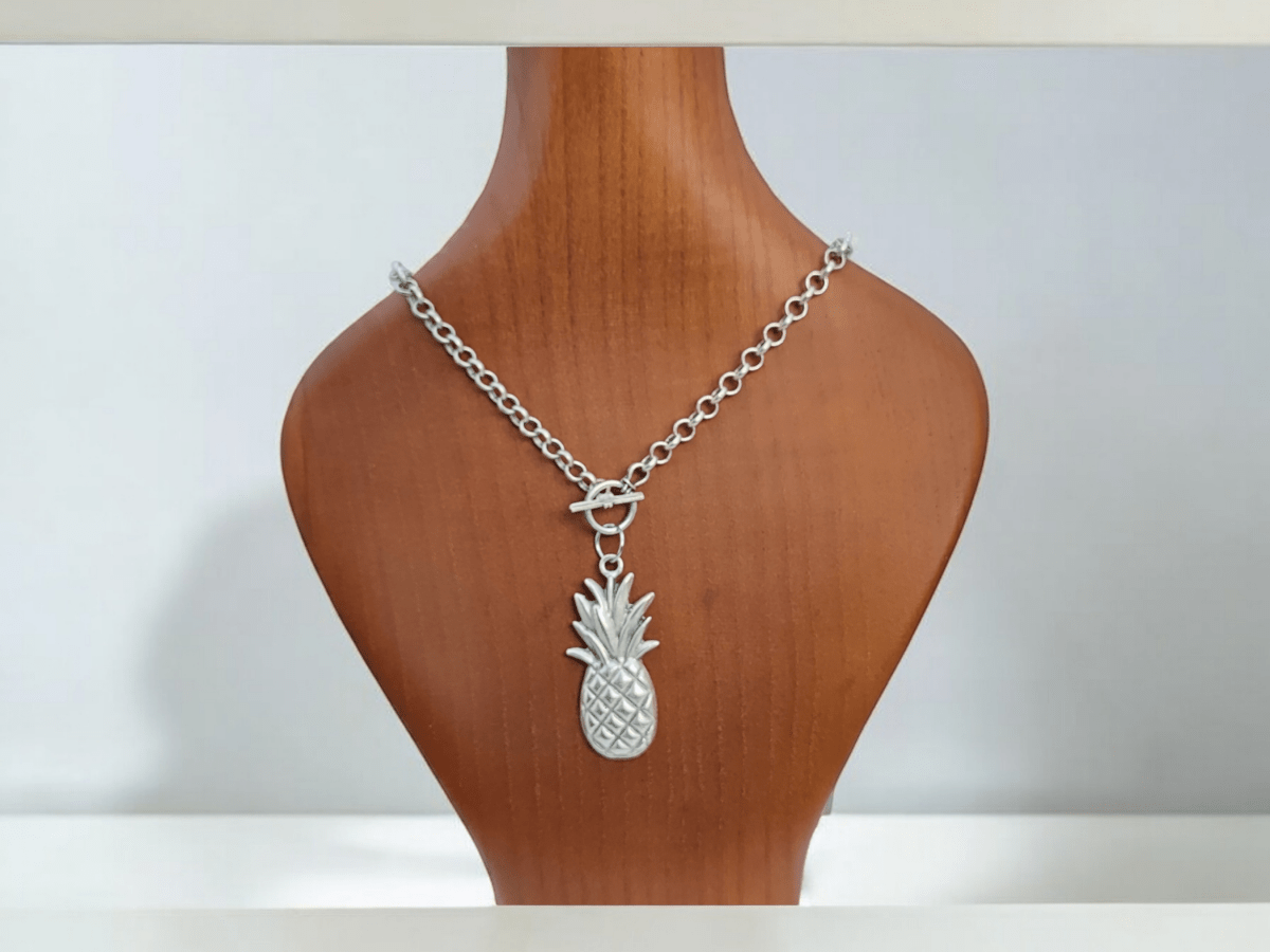 a pineapple silver charm necklace on a wooden bust