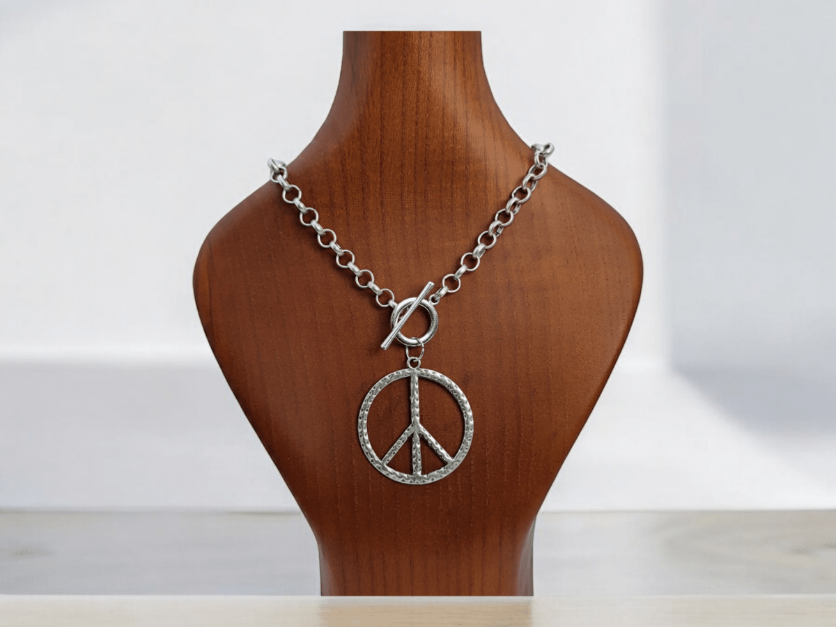 large peace symbol pendant on a silver chain on a wooden bust