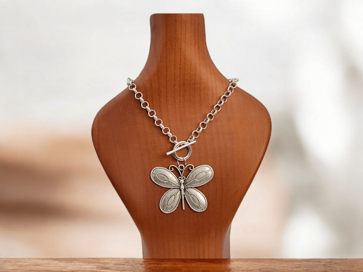 A large Silver butterfly on a silver chain on a wooden bust Main image