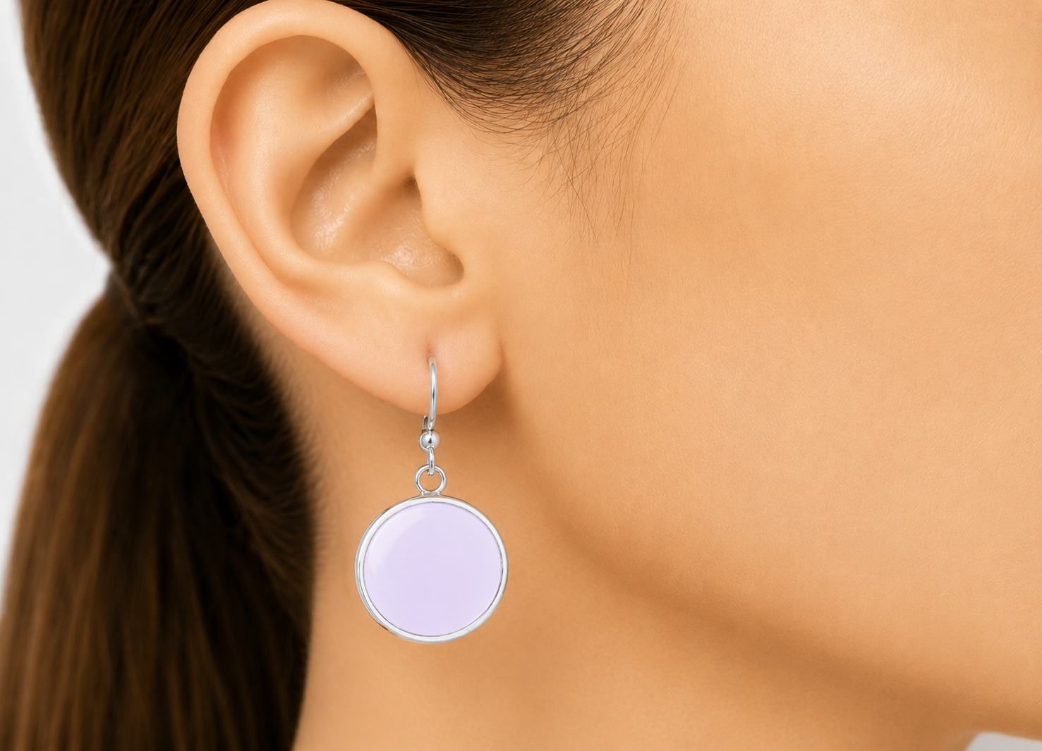 Close-up of an ear wearing a round purple earring with a blurred background
