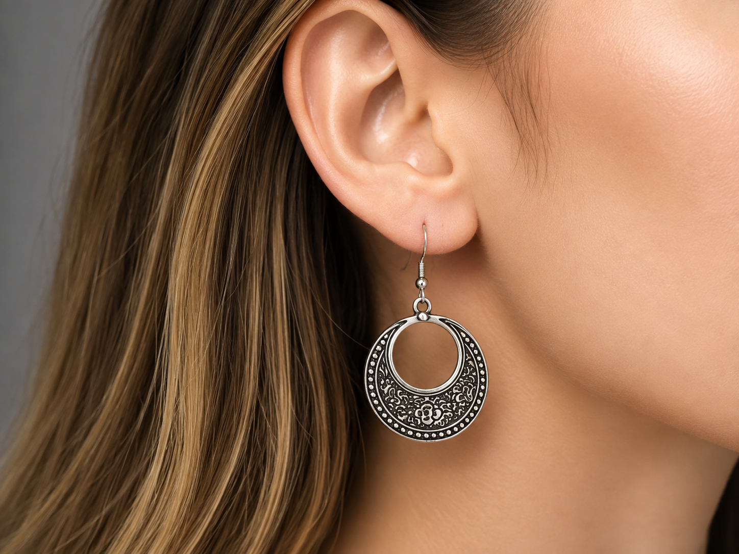 A close-up of a woman's ear wearing a silver crescent moon dangle earring with ornate filigree detailing. Main image
