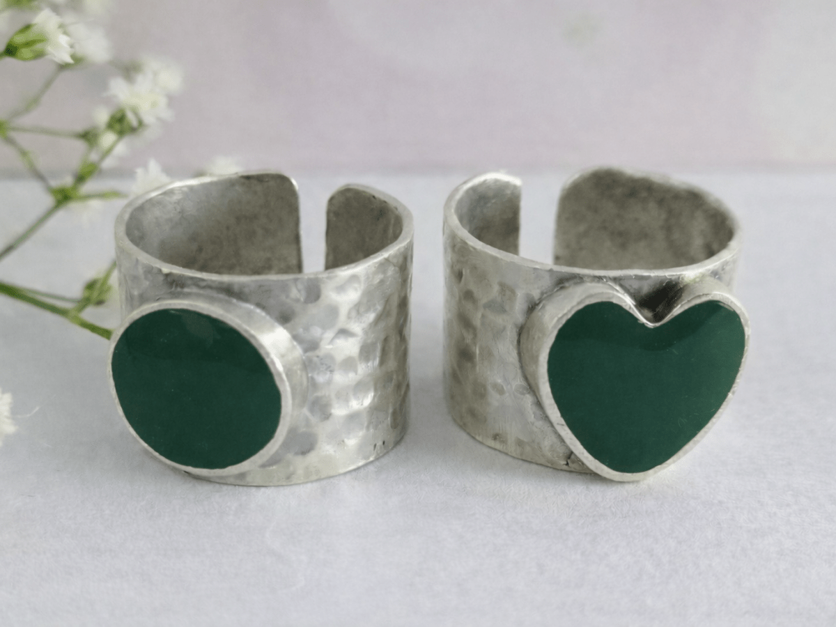 A picture of 2 bands rings, one with a dark green heart one with a dark green circle