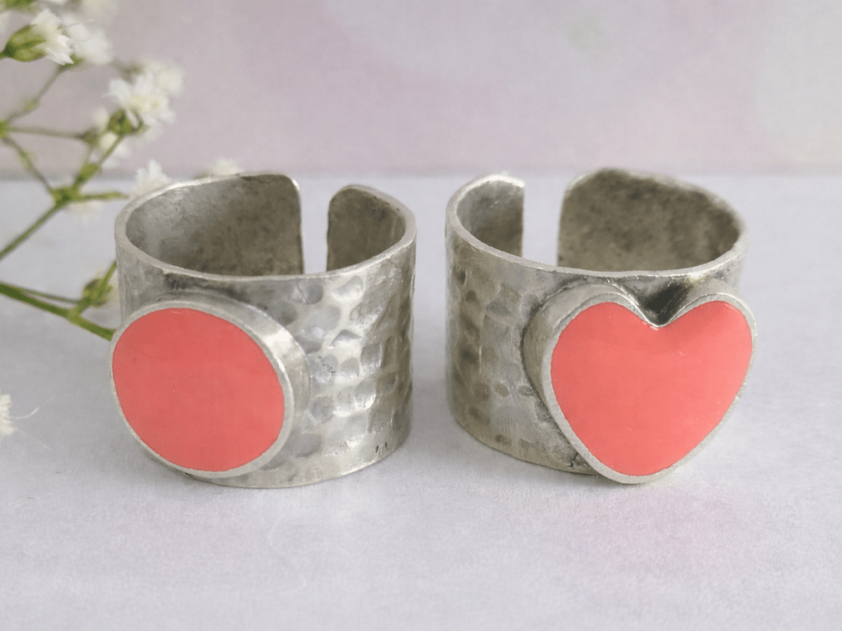 A picture of 2 bands rings, one with a salmon pink heart one with a salmon pink circle