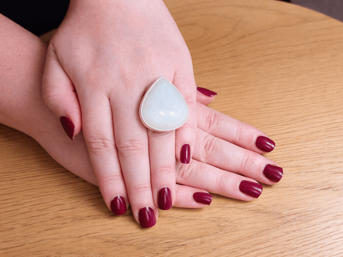 Hand wearing a teardrop-shaped ring on a wooden surface Main image