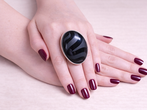 Hand wearing a large black ring with wavy design on a light background