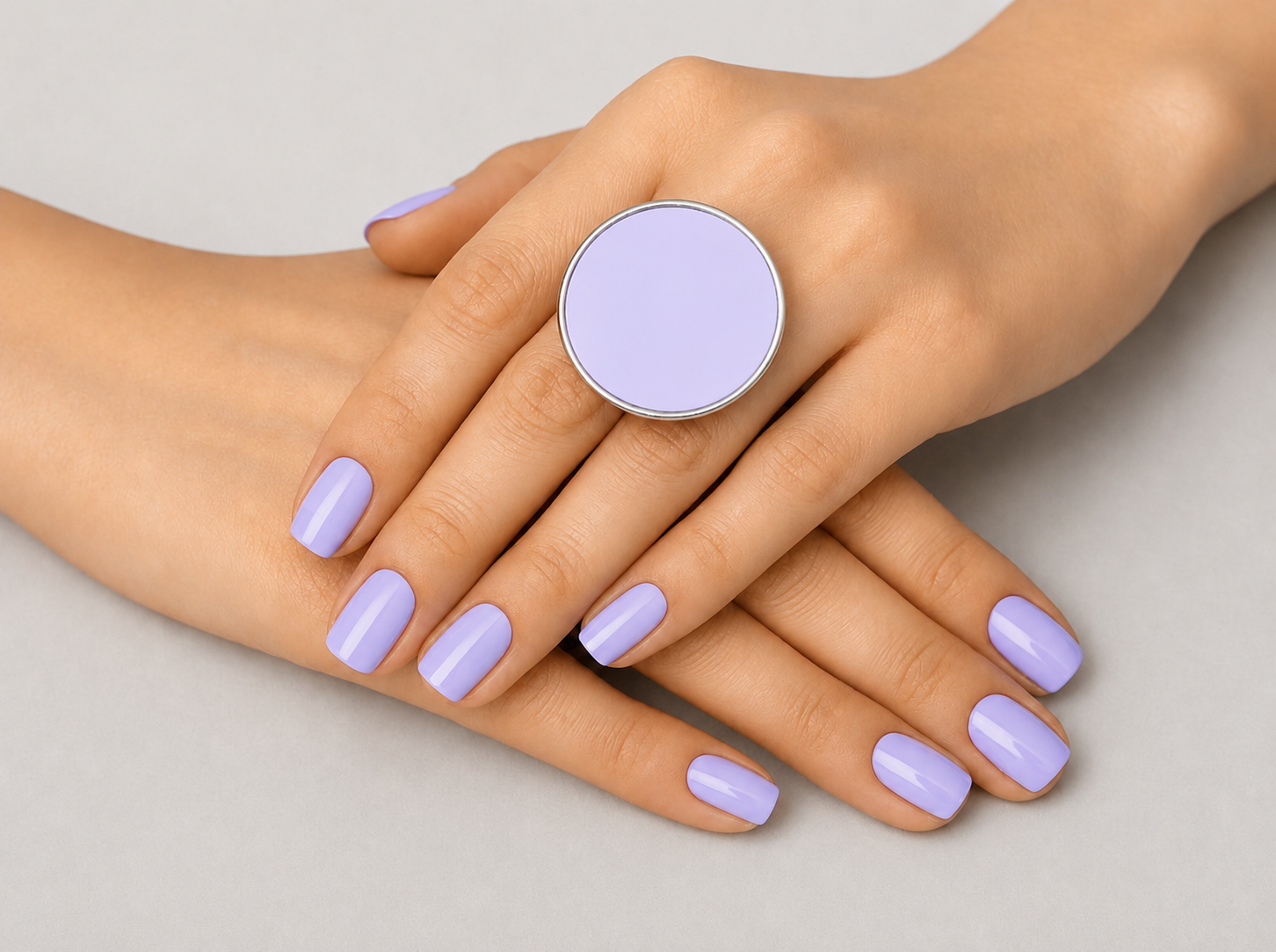 Hand wearing a lavender ring with matching nail polish on a neutral background Main image