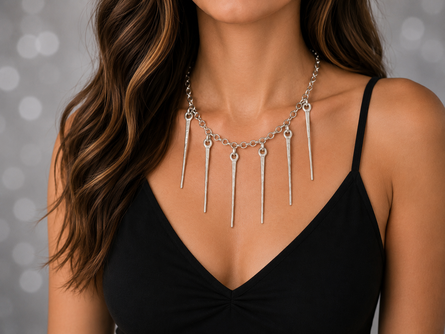 a close up of a model in a black strappy top wearing a silver necklace with silver fringe