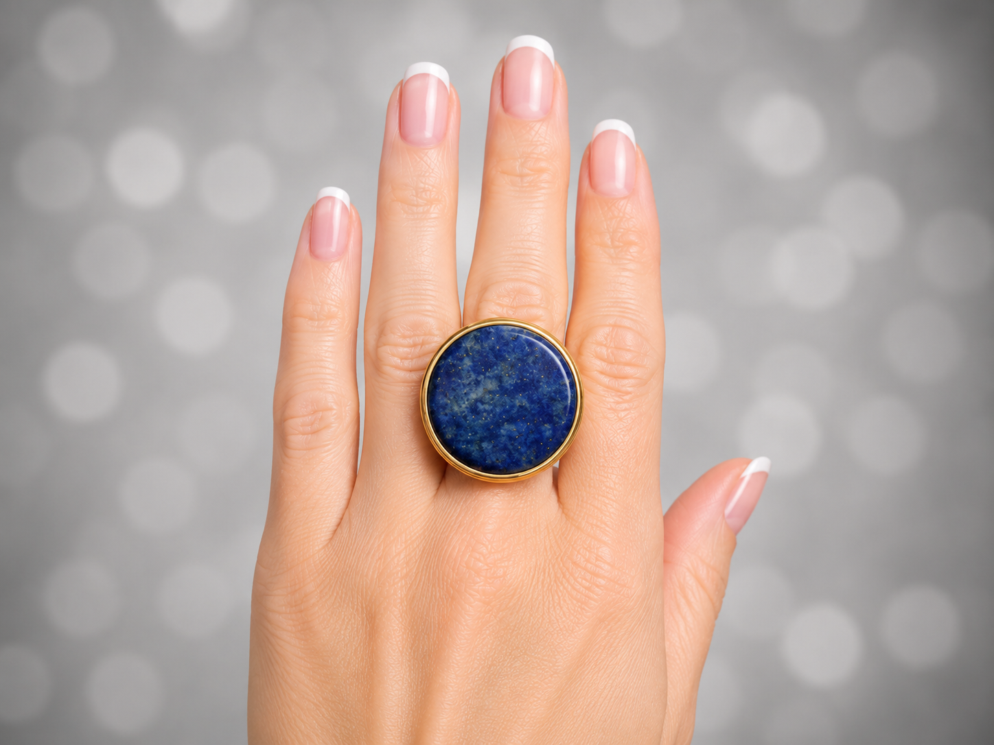 a close up of a models hand wearing a blue Lapis Lazuli ring against a grey bokhe background