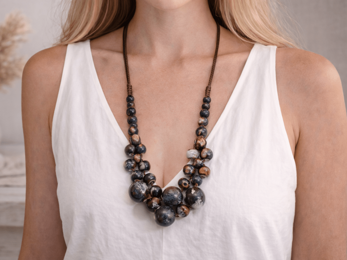 A model with a white top wearing a blue and bronze ceramic beaded necklace Main image