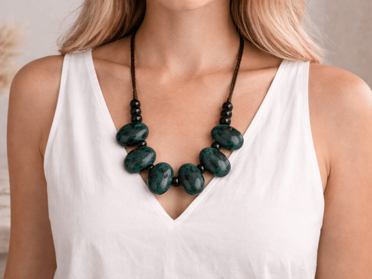 a model with a white top wearing a black and green ceramic necklace Main image