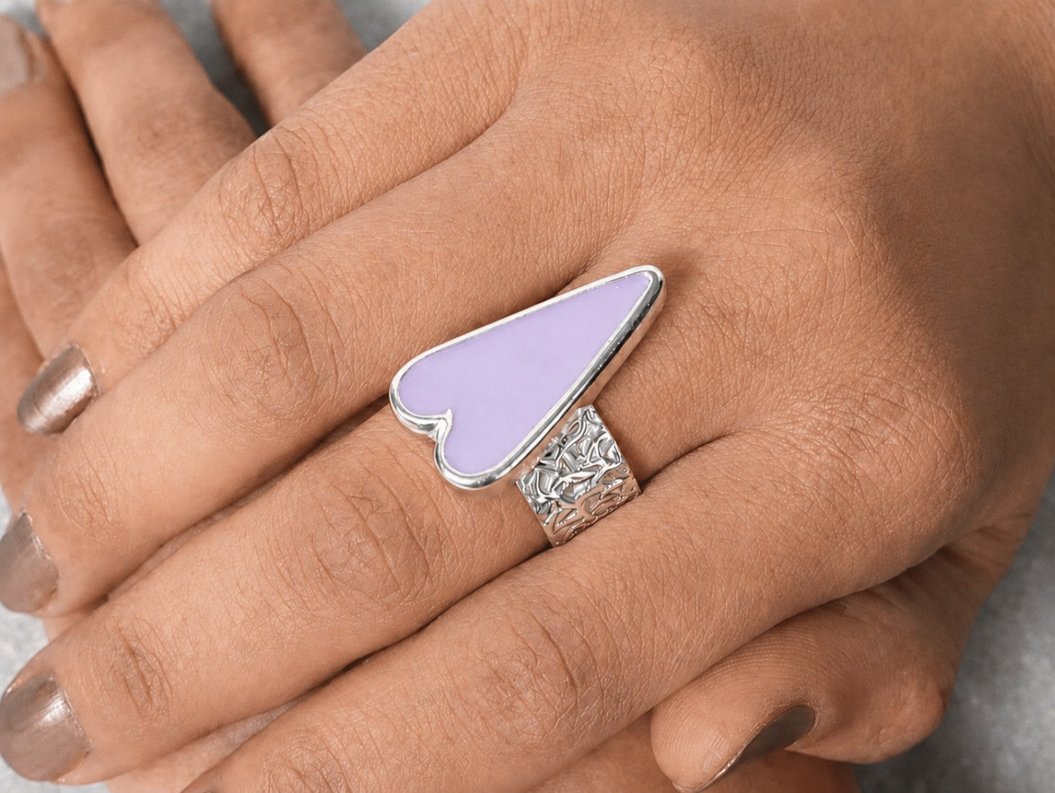 Hand wearing a silver ring with a purple stone on a neutral background Main image