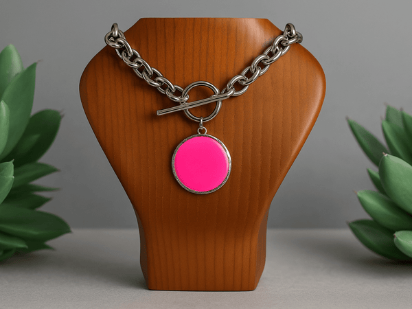 A large neon pink pendant on a chunky chain displayed on a wooden bust