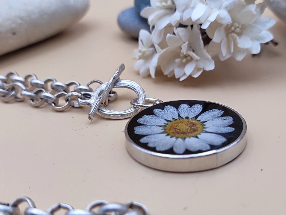 A black pendant with a dried daisy flower at the centre on a silver chain