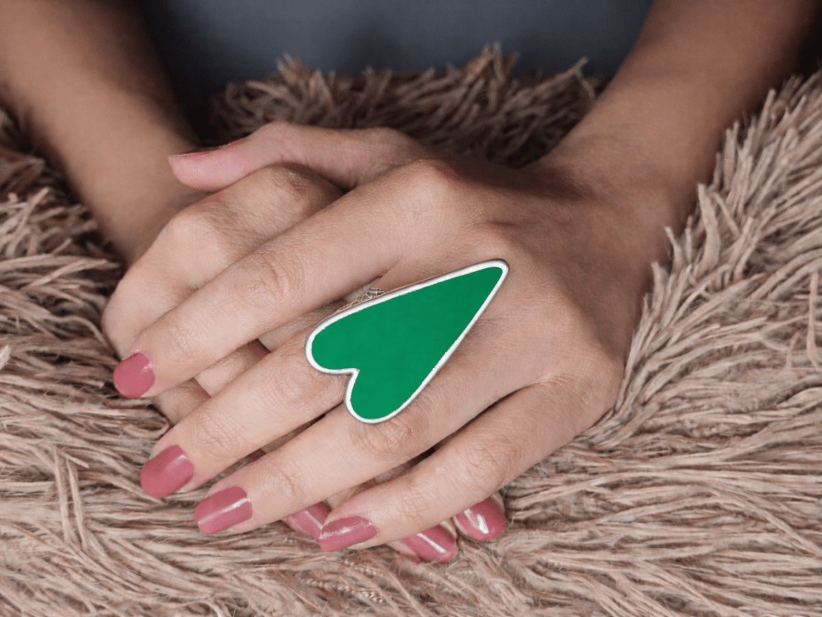 A models hand wearing a large bright green heart shaped ring
