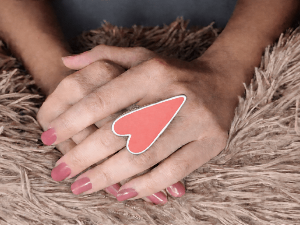 A models hand wearing a large salmon pink heart shaped ring