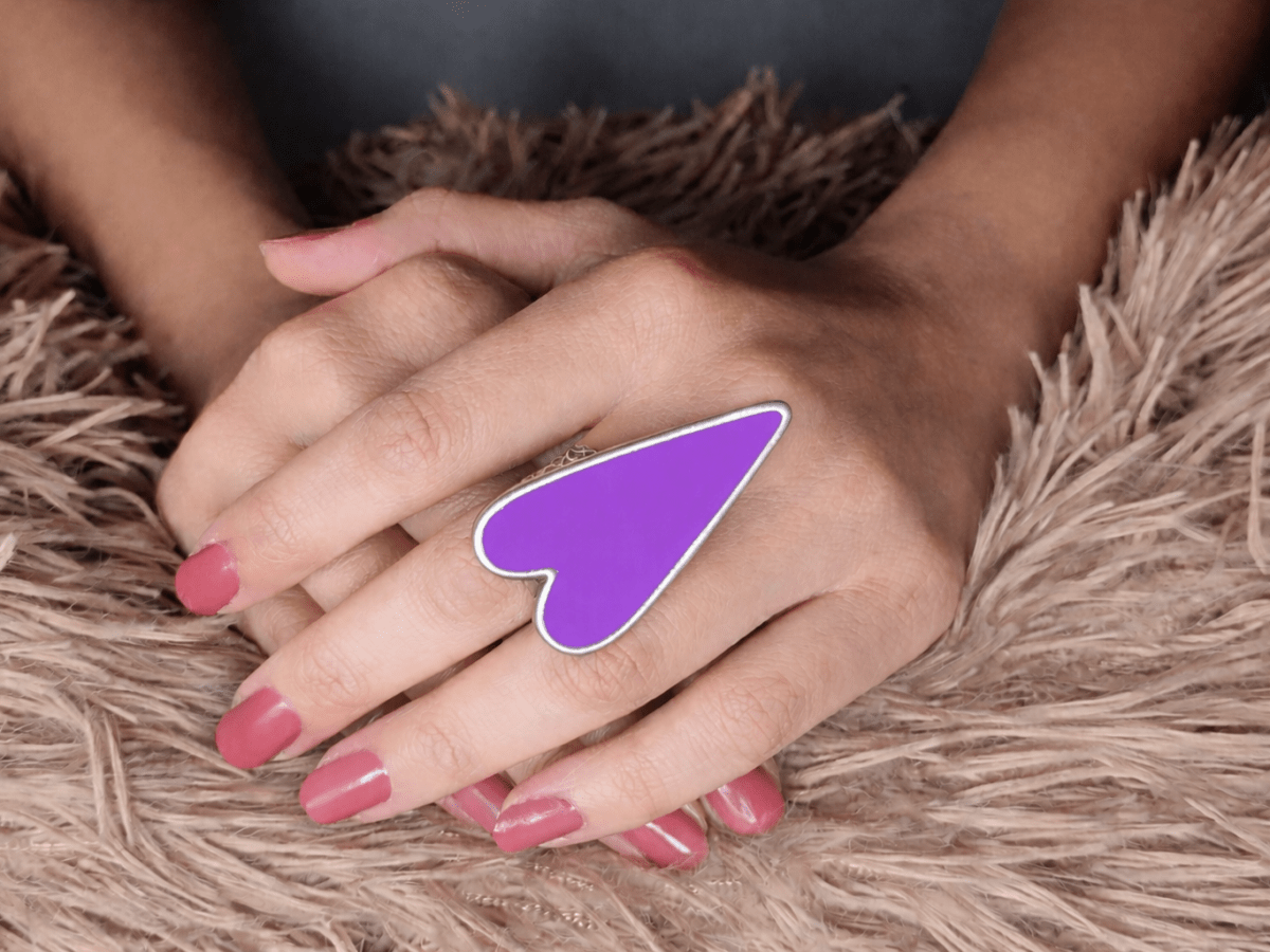 A models hand wearing a large violet heart shaped ring