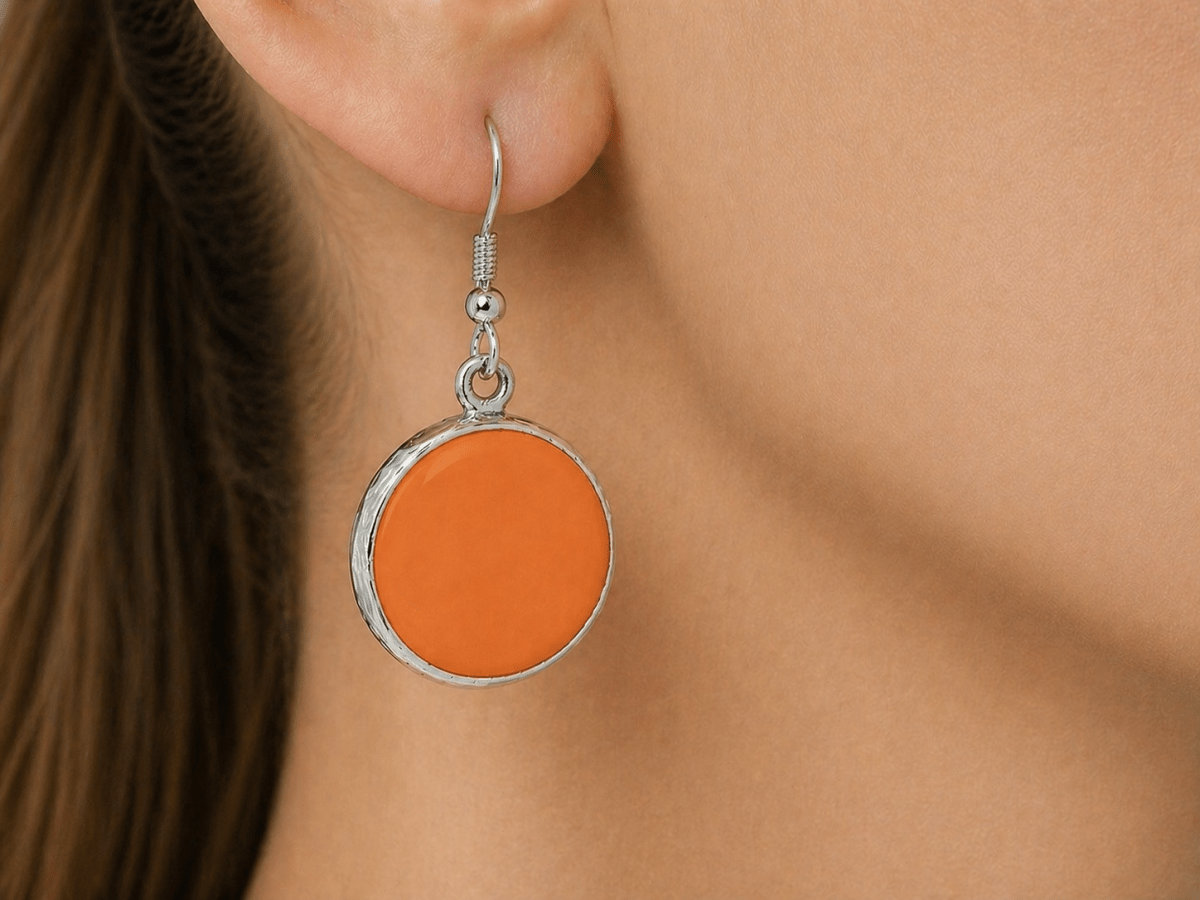 A model wearing some round orange dangle drop earrings