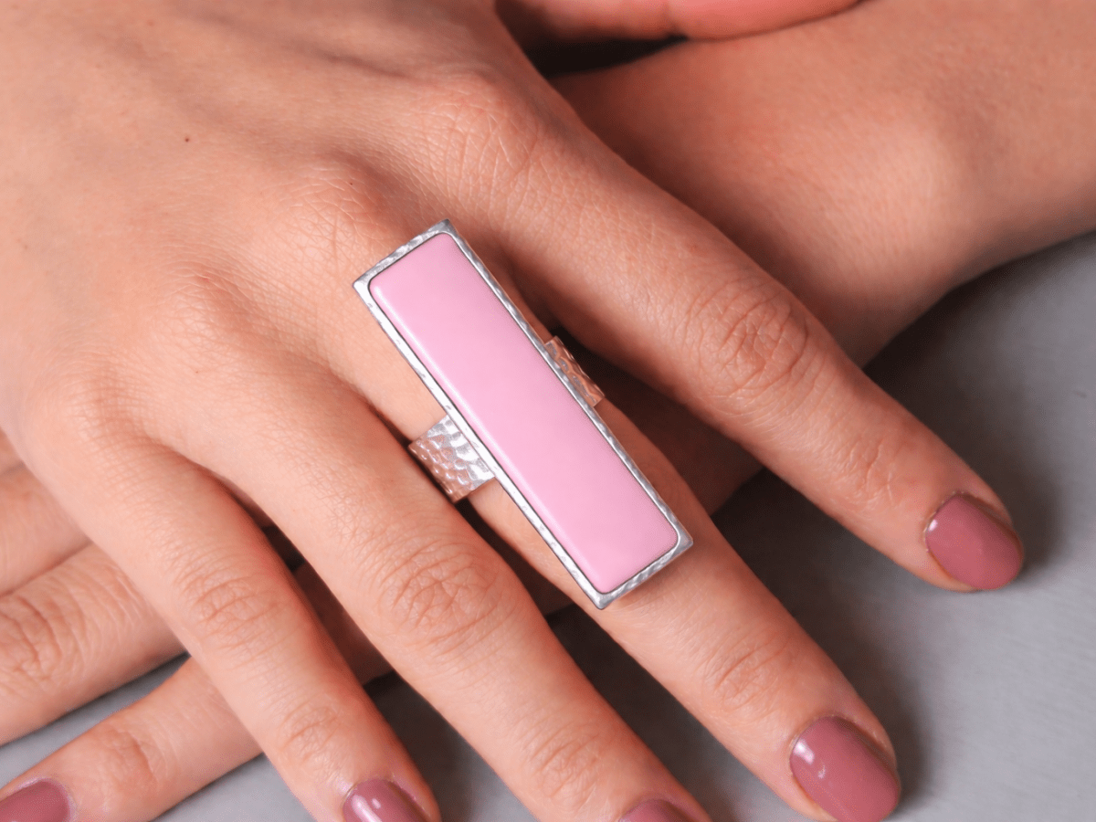 A models hand wearing a long narrow pink  ring with silver band