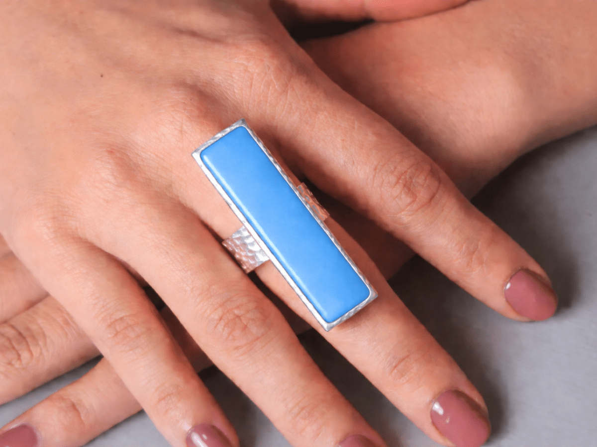 A models hand wearing a long narrow blue ring with silver band