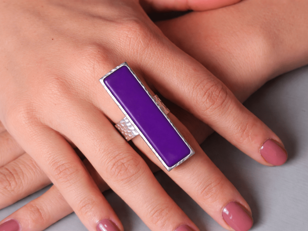 A models hand wearing a long narrow purple ring with silver band