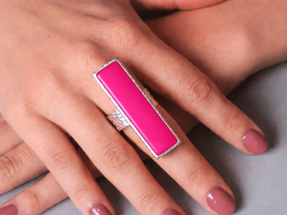 A models hand wearing a long narrow deep pink ring with silver band