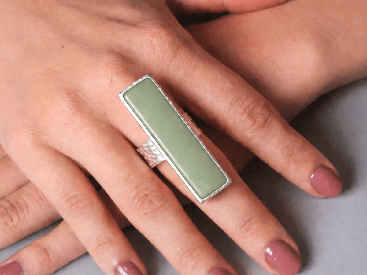 A models hand wearing a long narrow sage green ring with silver band