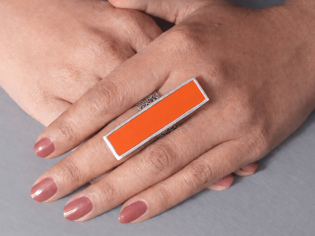 A models hand wearing a long slim orange ring