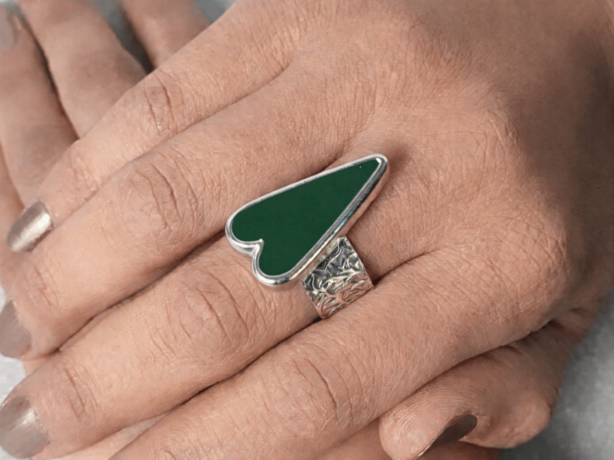 A models hands wearing a dark green heart ring