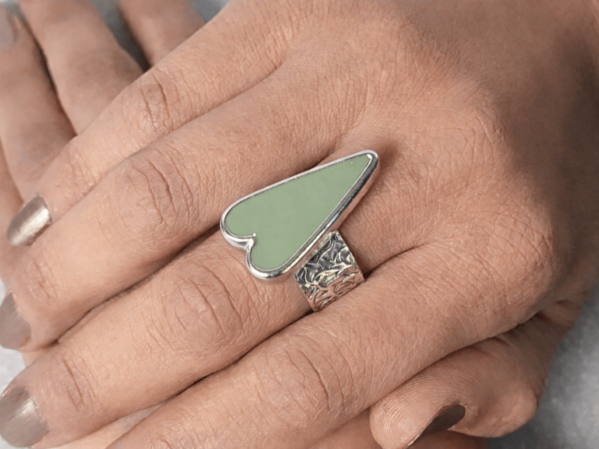 A models hands wearing a sage green heart ring