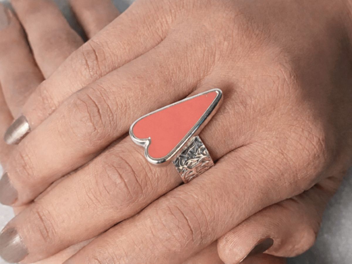 A models hands wearing a salmon pink heart ring