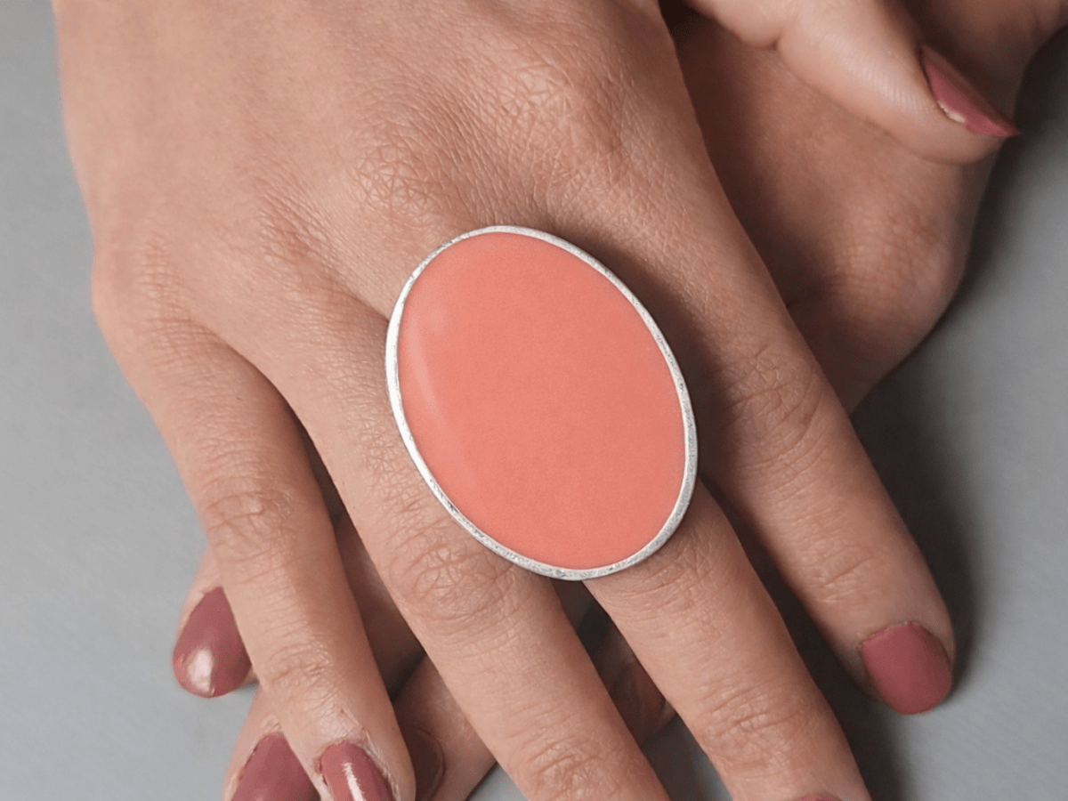 A models hands wearing a large salmon pink oval ring