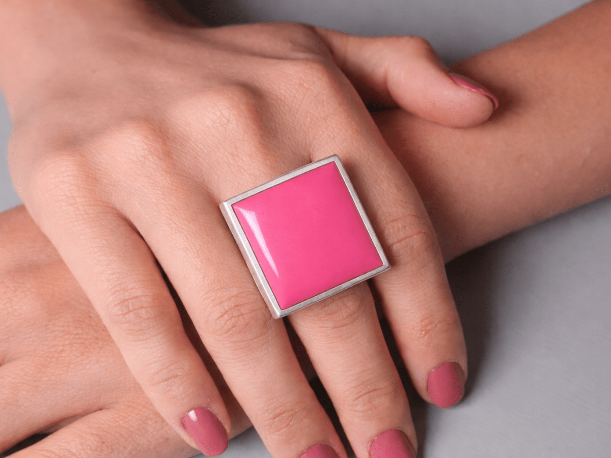 Models hands wearing a square deep pink ring