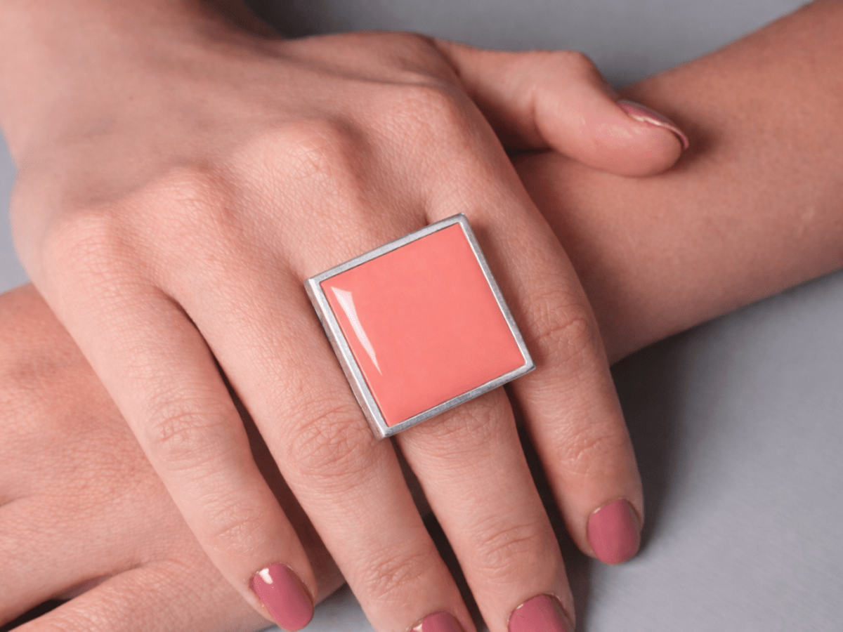Models hands wearing a square salmon pink ring