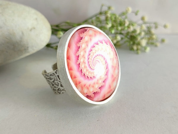 a pink ring on a grey surface surrounded y stones and flowers